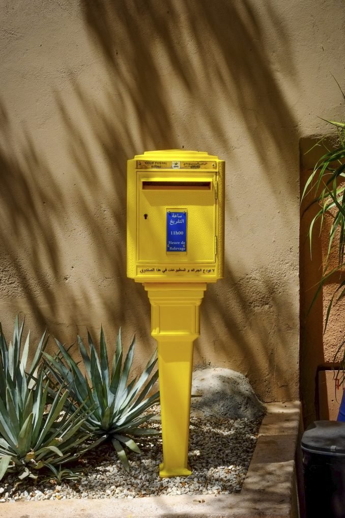 Yellow and blue postbox in dappled sunlight