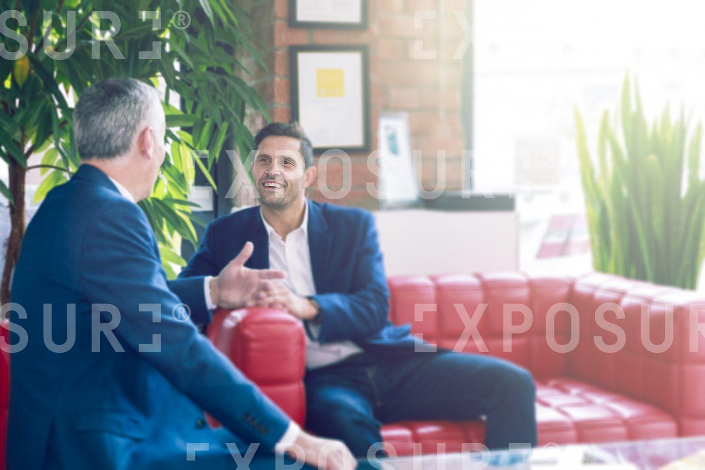 Two Businessmen Chatting On Red Sofa